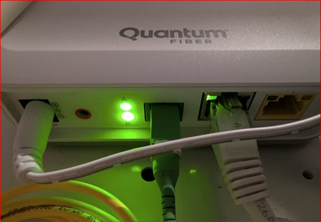Back of a white Quantum Fiber box. Power is plugged in on the left. A green fiber connector is in the center. One Ethernet port has a white cable with a green link light. The Ethernet port to the right is empty and yellow inside.